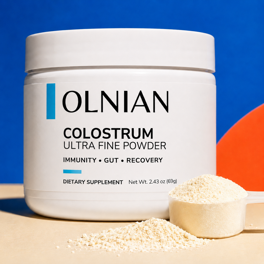 A white plastic tub of OLNIAN Colostrum Powder dietary supplement, shown with a scoop and loose powder in front, set against a blue background with a beige surface.