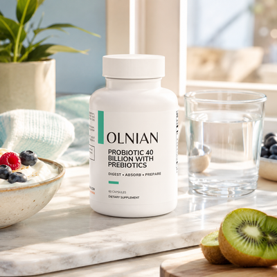 A white bottle of OLNIAN Probiotic 40 Billion With Prebiotics stands on a marble countertop in a bright kitchen setting, surrounded by a glass of water, yogurt with berries, and sliced kiwi.