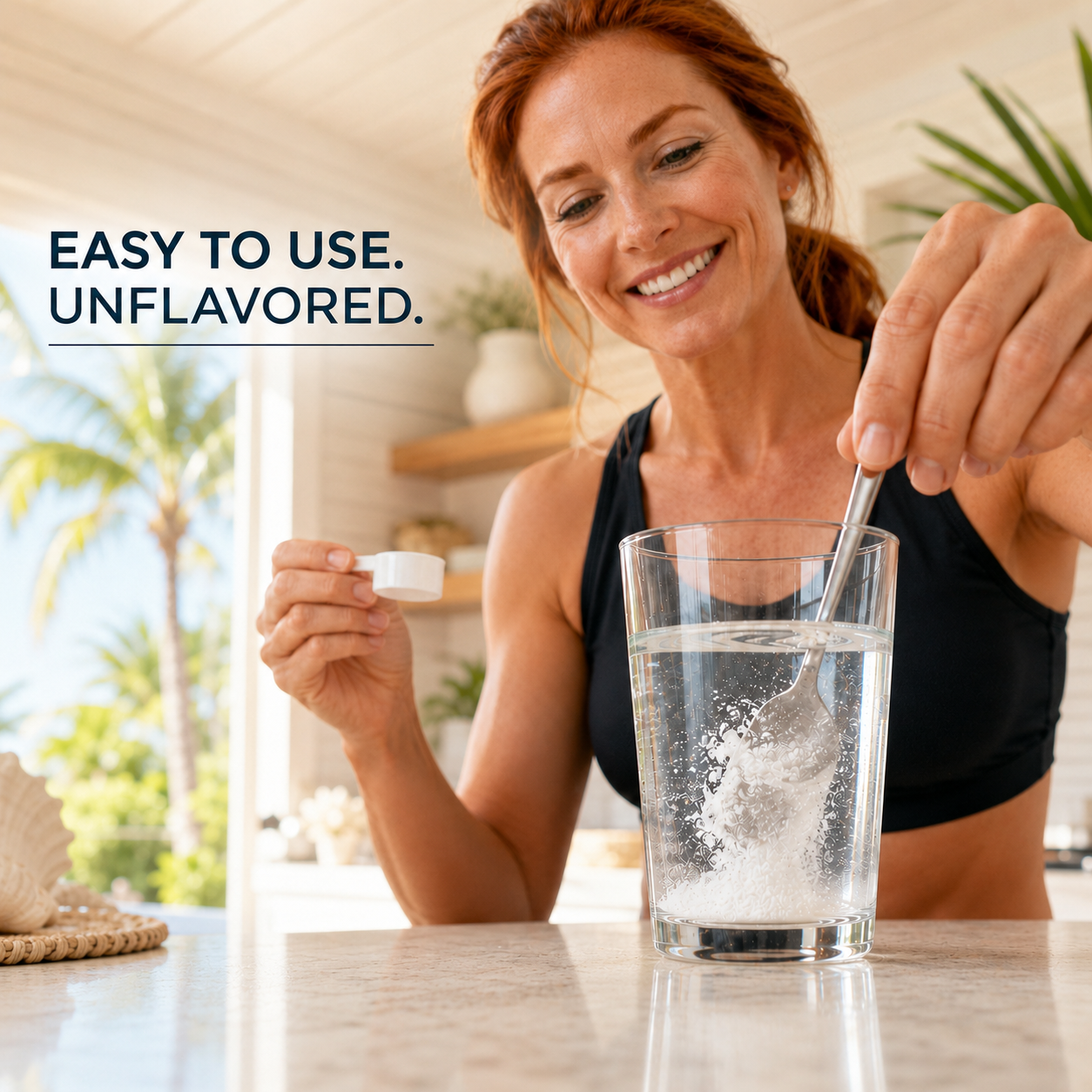 A smiling woman in a black sports bra stands at a kitchen counter, mixing white powder into a glass of water with a spoon. She holds a small white cap in her other hand.